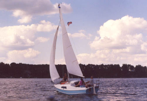 A twenty foot sailboat, Anungoday, under full sail, with three people aboard, on a sunny day.